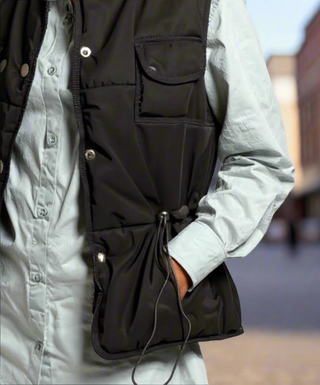 Person wearing a black vest over a light gray shirt with a blurred background